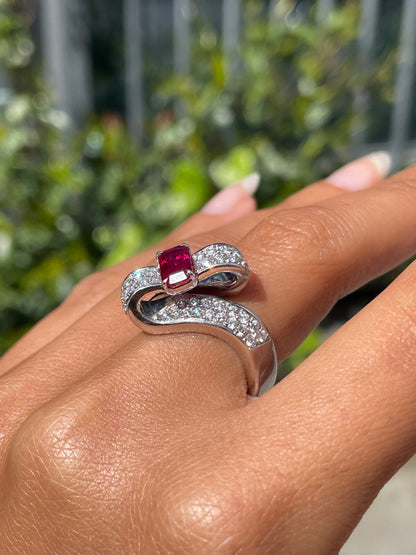 18ct white gold twisted ribbon dress ring with 1.04ct emerald cut ruby centre and 1.30ct round brilliant cut diamonds inlaid in two rows on hand