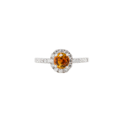 An 18K white gold cluster engagement ring with a round orange sapphire center stone and a halo of round brilliant cut diamonds.