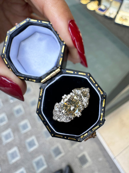 A vintage platinum engagement ring with a central 1.18ct fancy brown round brilliant cut diamond and three rose cut diamonds on either side, set in leaf designed pierced shoulders in box