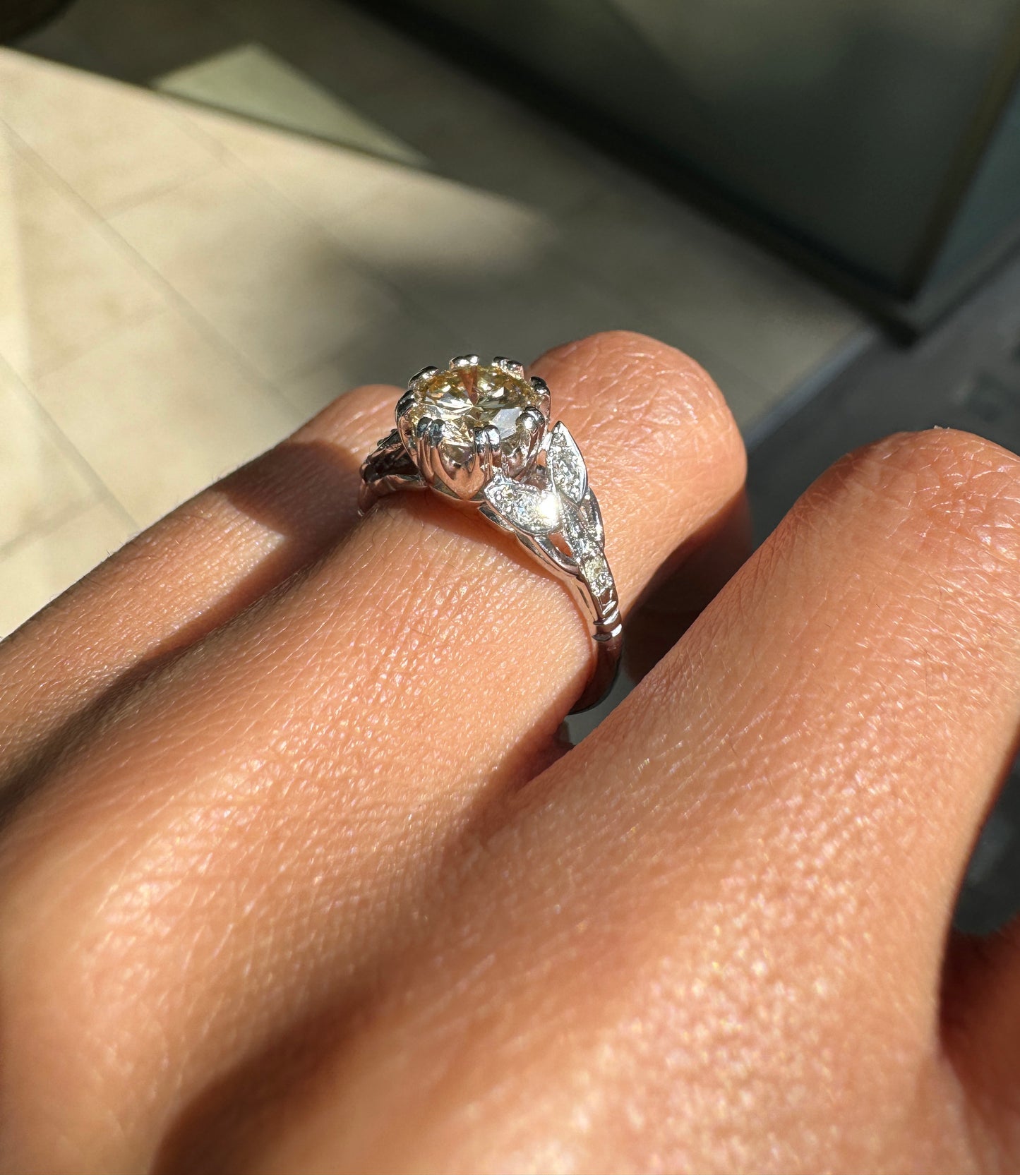A vintage platinum engagement ring with a central 1.18ct fancy brown round brilliant cut diamond and three rose cut diamonds on either side, set in leaf designed pierced shoulders on hand