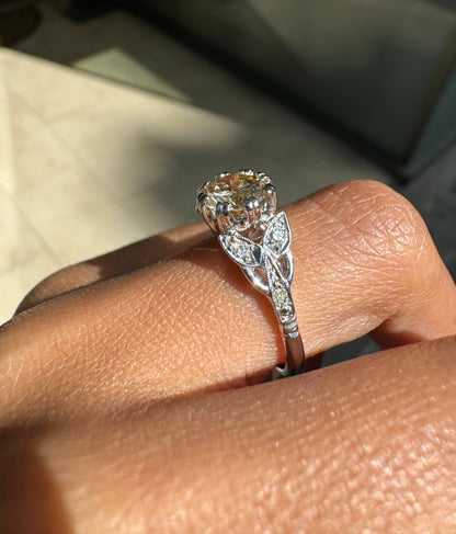 A vintage platinum engagement ring with a central 1.18ct fancy brown round brilliant cut diamond and three rose cut diamonds on either side, set in leaf designed pierced shoulders on hand