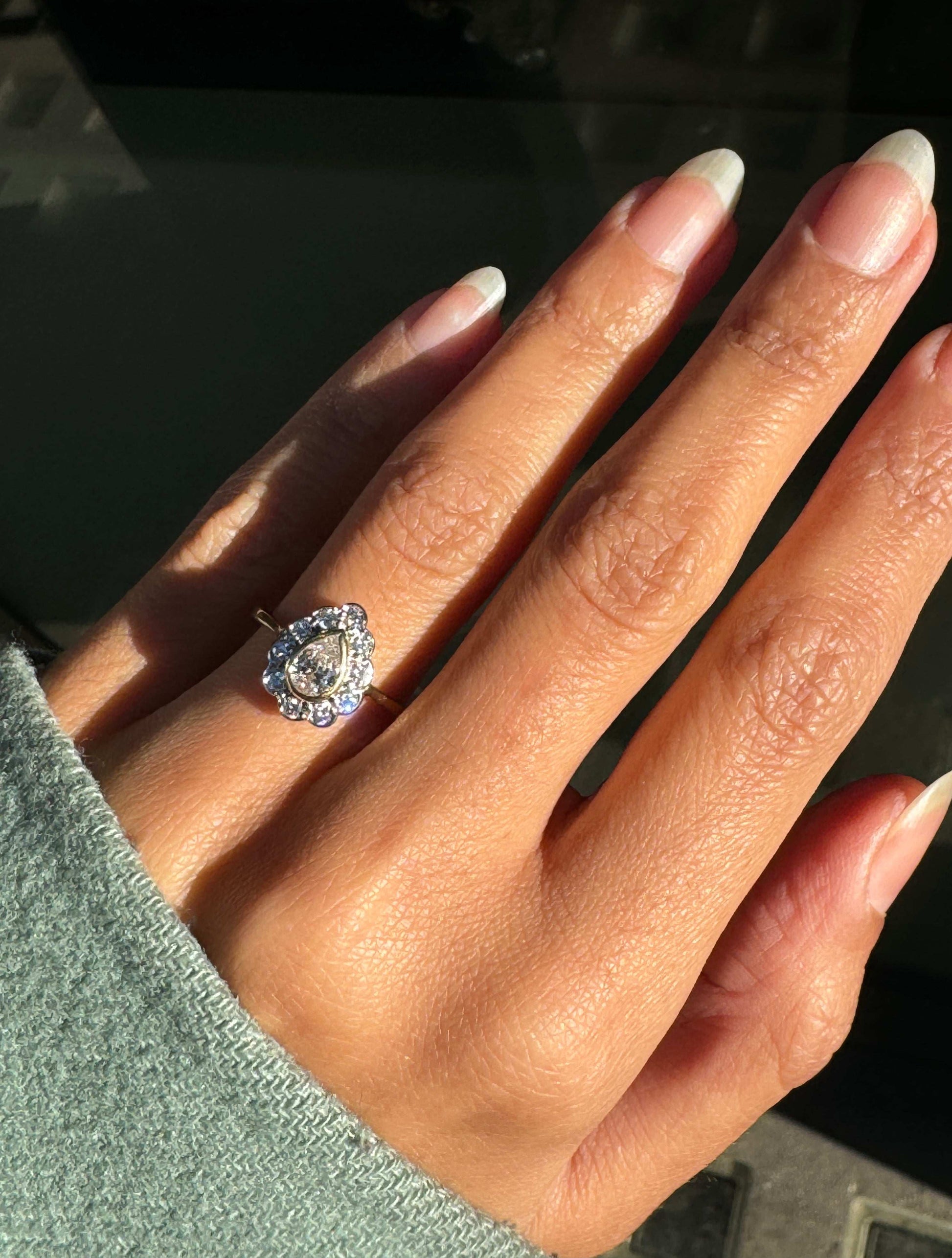 An 18 carat white and yellow gold pear shape diamond coronet cluster engagement ring with a central diamond surrounded by a halo of round brilliant cut diamonds on hand