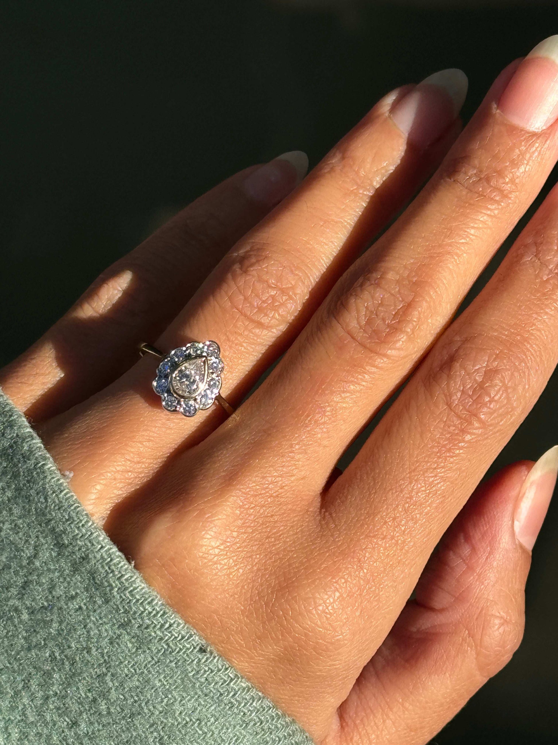  An 18 carat white and yellow gold pear shape diamond coronet cluster engagement ring with a central diamond surrounded by a halo of round brilliant cut diamonds on hand