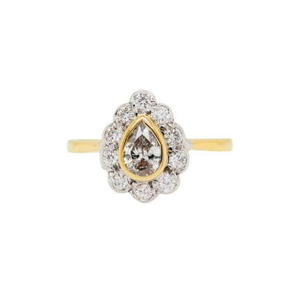 An 18 carat white and yellow gold pear shape diamond coronet cluster engagement ring with a central diamond surrounded by a halo of round brilliant cut diamonds.