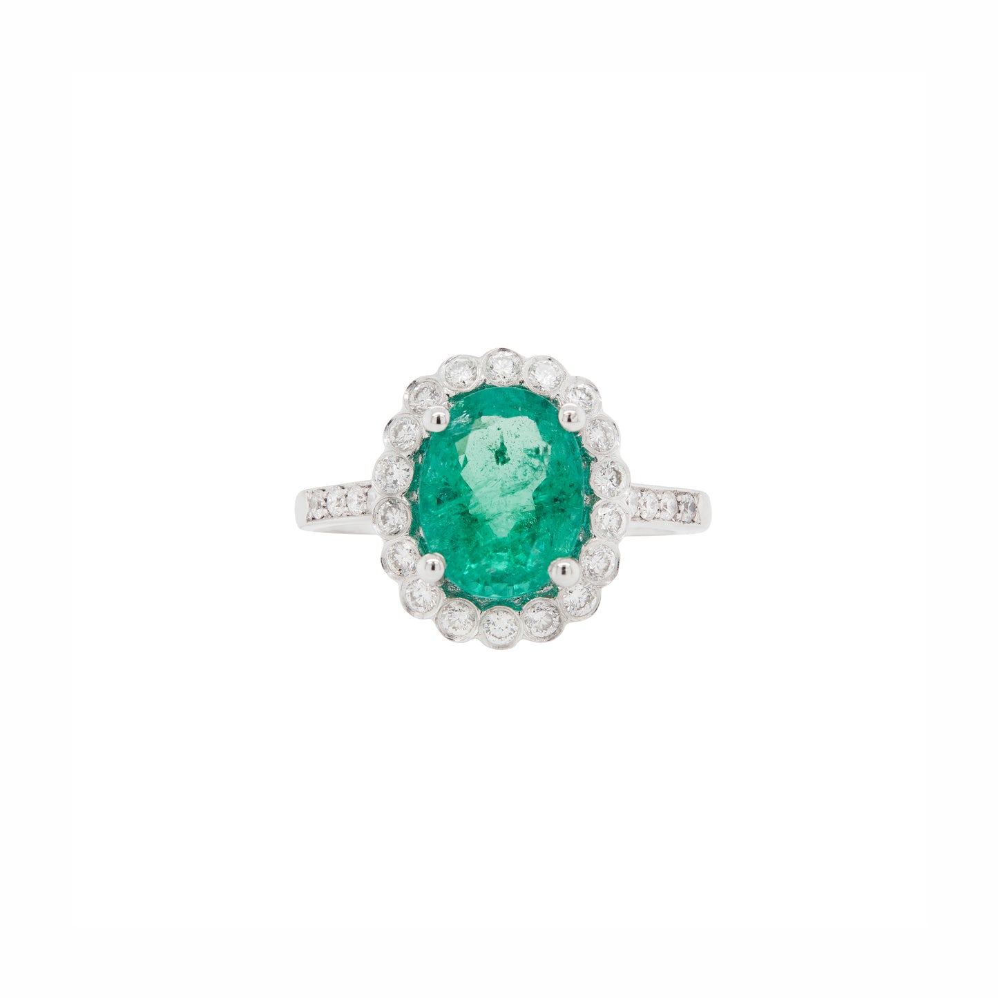 An 18 carat white gold cluster engagement ring with a central oval emerald and a halo of round brilliant cut diamonds.