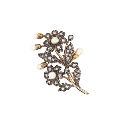An antique floral brooch with pearl accents and rose cut diamonds, predominantly silver in color with a gold base, from the late 1800s.