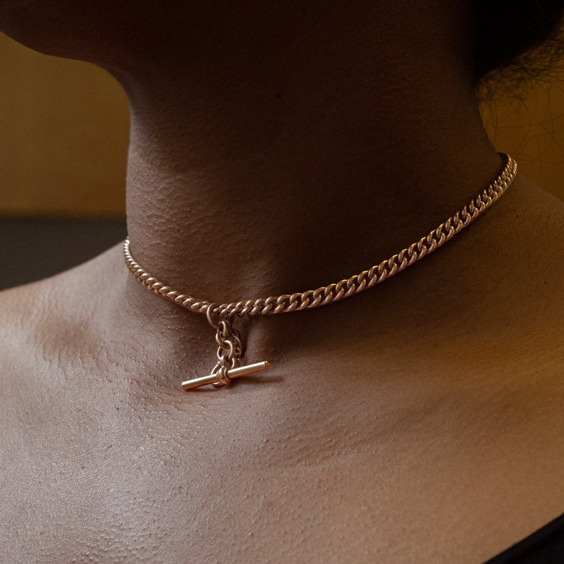 A rose gold antique Albert chain necklace with two lobster clasps and a T-bar and bolt ring on neck
