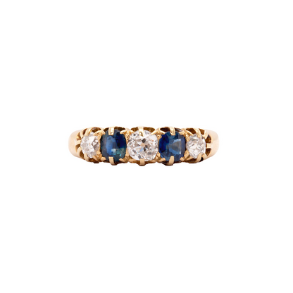 An 18ct yellow gold five-stone ring featuring three old cut diamonds and two deep blue sapphires, claw set in a fluted gallery.