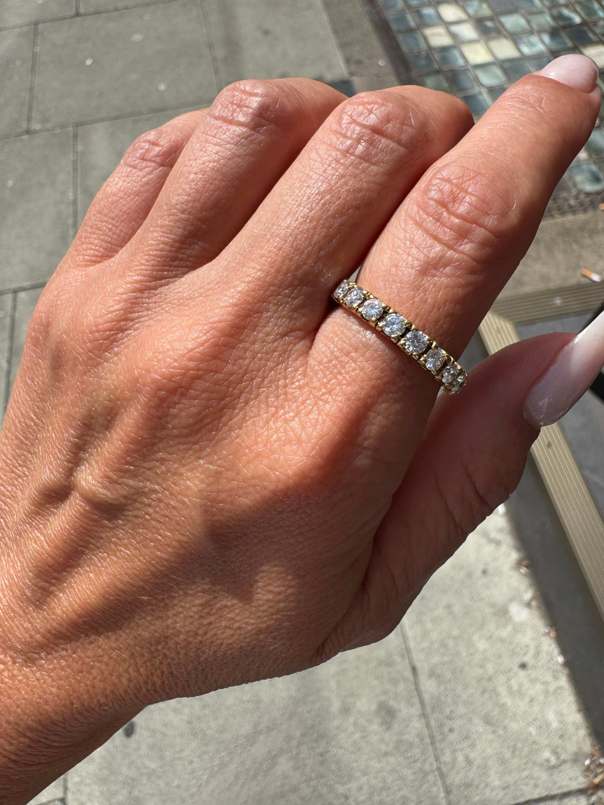 Hand wearing a diamond ring on a blurred outdoor background