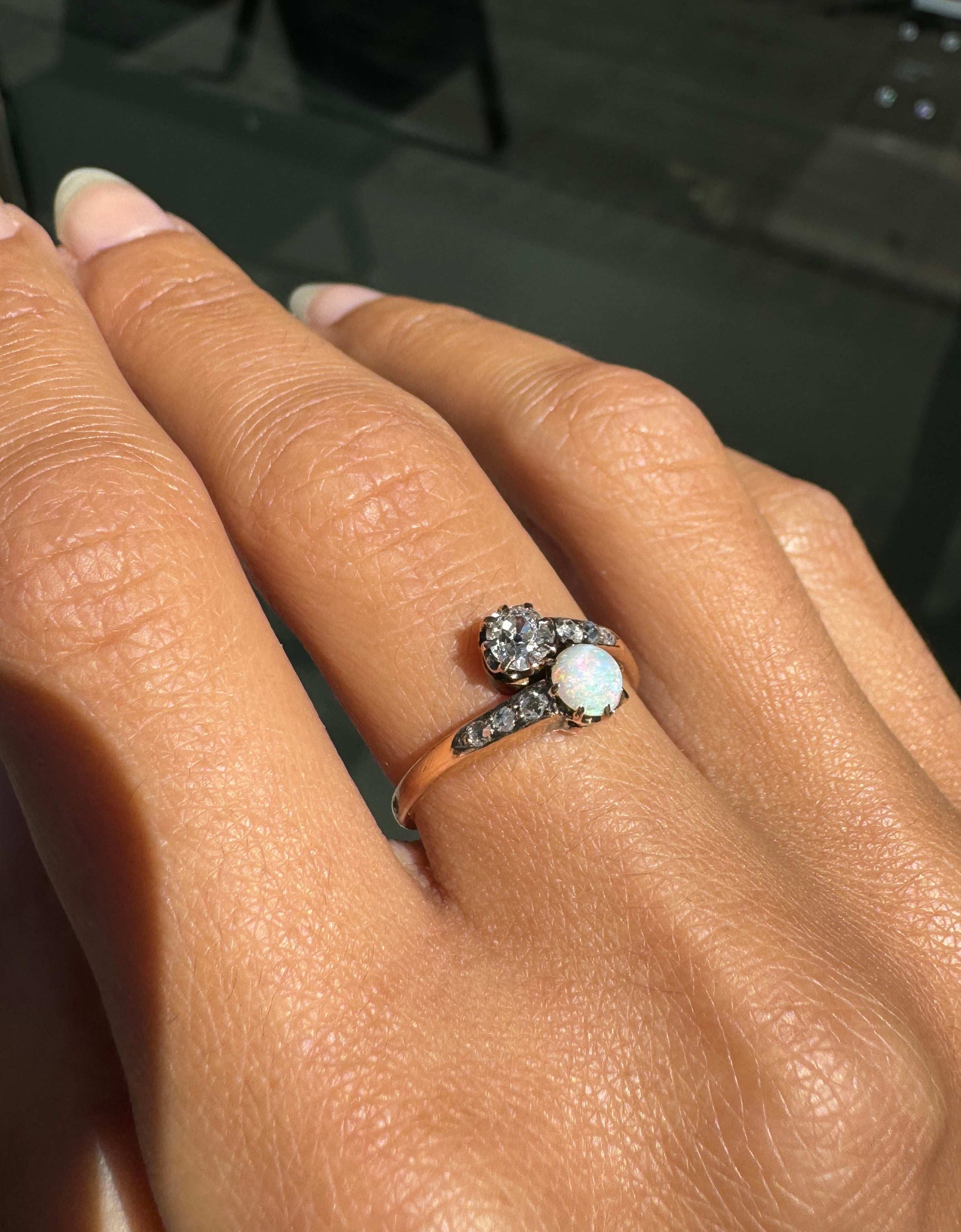 Ring with a central gemstone and smaller diamonds on a hand against a dark background
