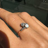 Close-up of a hand wearing an ornate ring with a central gemstone on a blurred background