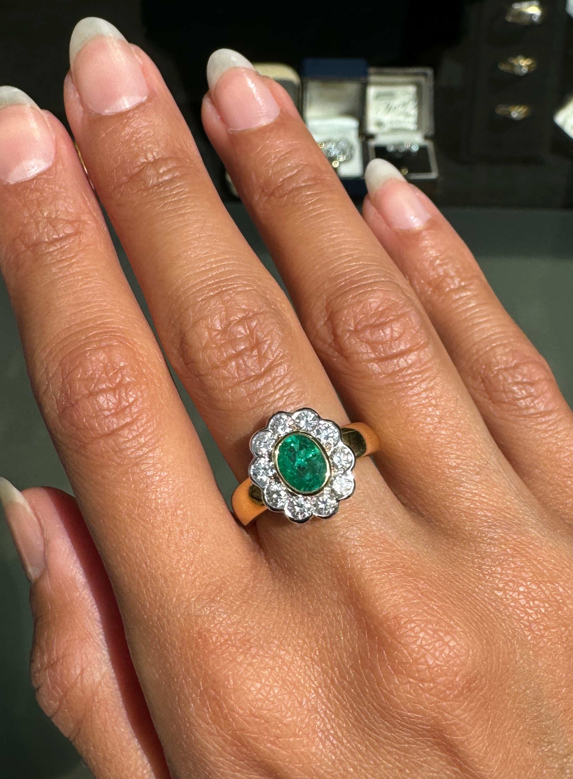 Hand wearing a ring with an emerald and diamonds, with a blurred background