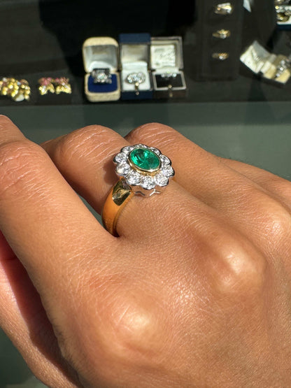 Gold ring with a green gemstone on a hand, with jewelry display in the background.