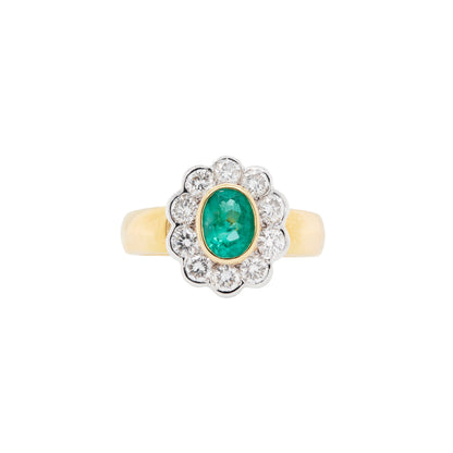 An oval emerald ring with a diamond halo, set in a cluster design with yellow and white gold.