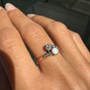 Ring with a central gemstone and smaller diamonds on a hand against a dark background