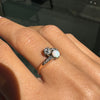Close-up of a hand wearing an ornate ring with a central gemstone on a blurred background