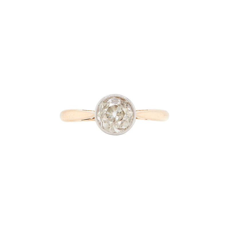 An Art Deco style solitaire diamond ring with a rub-over setting, featuring a millgrain edge on the band, photographed on a white background.