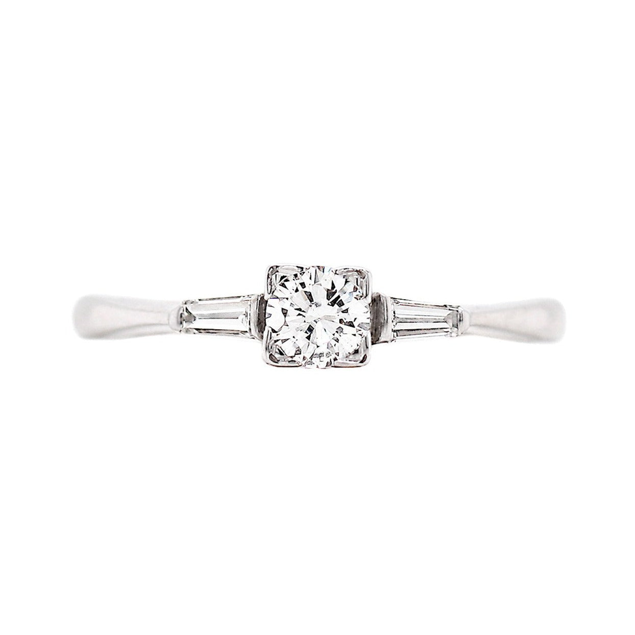 An engagement ring featuring a round brilliant cut diamond centerpiece, flanked by two baguette cut diamonds, set in 18 carat white gold.