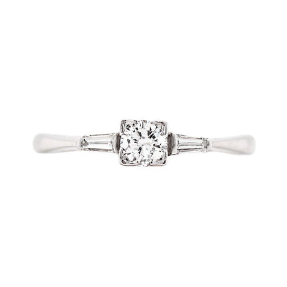 An engagement ring featuring a round brilliant cut diamond centerpiece, flanked by two baguette cut diamonds, set in 18 carat white gold.