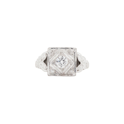 An antique Art Deco diamond and platinum hand carved cluster dress ring with a central round brilliant cut diamond and smaller eight cut diamonds on the corners, set within a square platinum frame with leaf motifs on the band.
