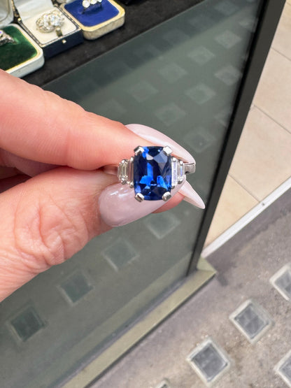 Hand holding a ring with a blue gemstone in front of a glass display case.