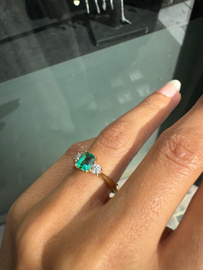 Close-up of a hand wearing a ring with a green gemstone on a reflective surface.