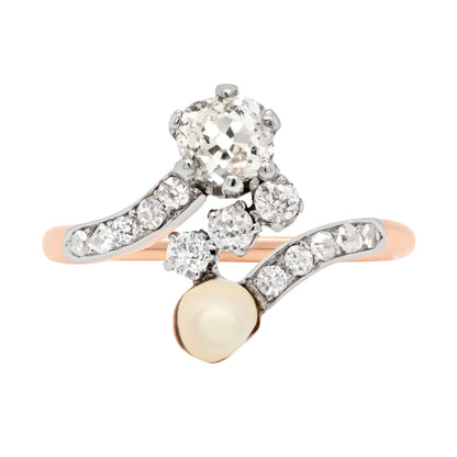 An antique engagement ring featuring a central diamond, flanked by two smaller diamonds and a pearl, all set in platinum on a rose gold mount.