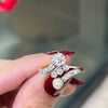 An antique engagement ring featuring a central diamond, flanked by two smaller diamonds and a pearl, all set in platinum on a rose gold mount on hand