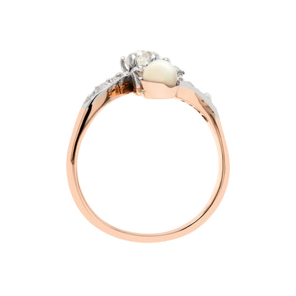 top view of An antique engagement ring featuring a central diamond, flanked by two smaller diamonds and a pearl, all set in platinum on a rose gold mount.