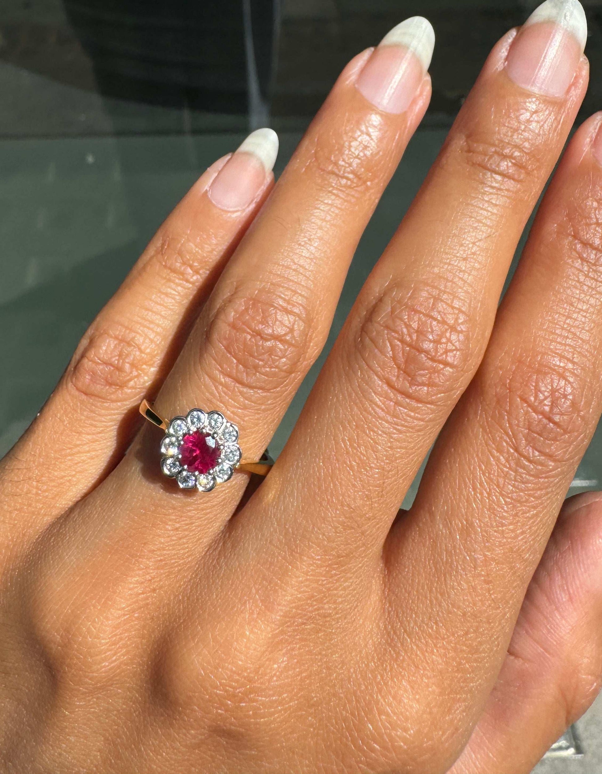 Close-up of a hand wearing a ring with a red ruby gemstone and diamonds