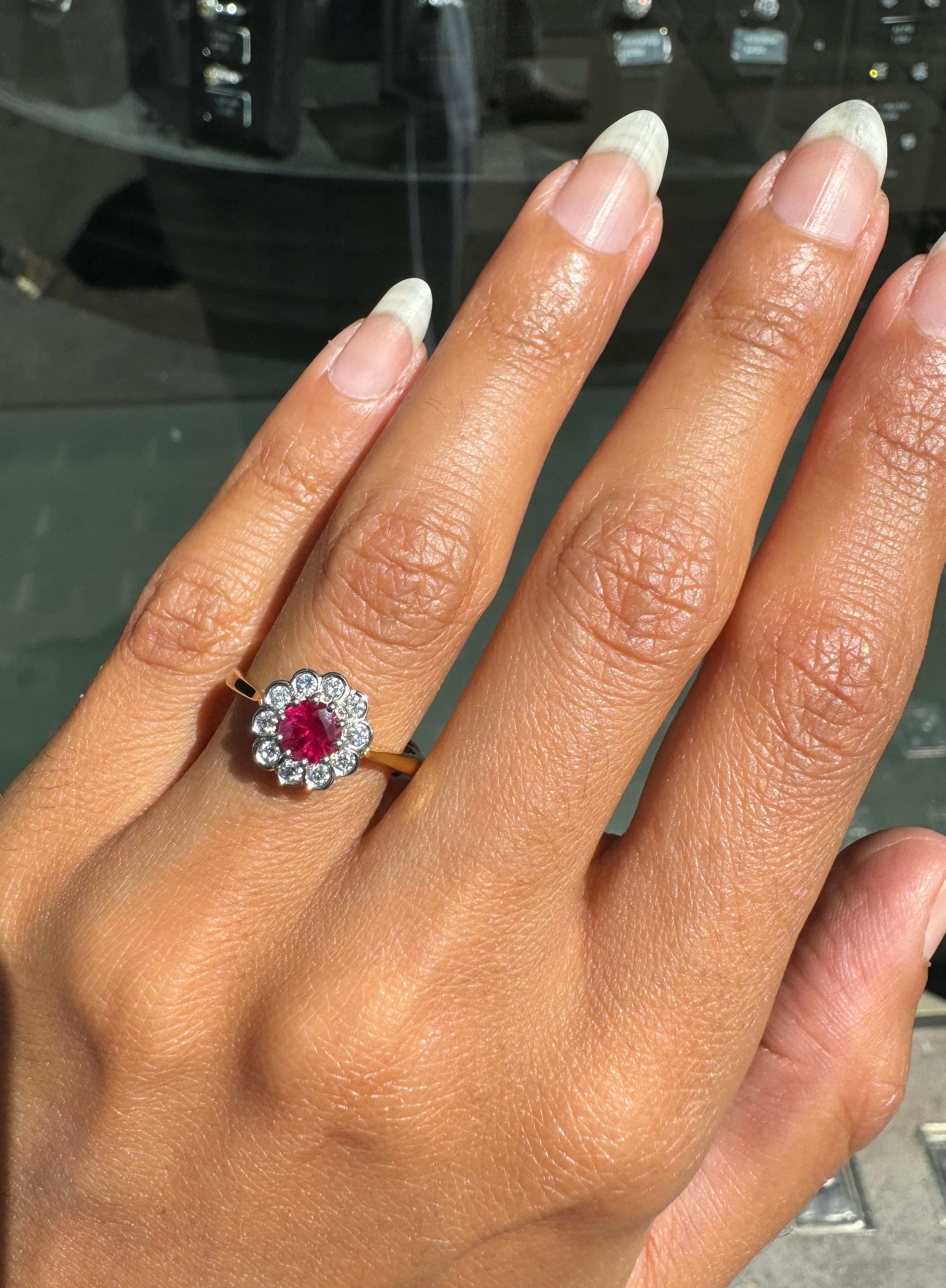 Hand wearing a ring with a red ruby gemstone, diamonds and a fine gold band