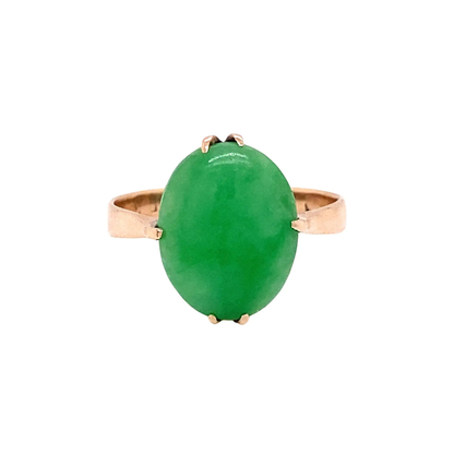 A vintage dress ring with a vivid green oval cabochon jadeite center stone held by a rose gold band.
