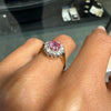 Ring with a pink gemstone on a finger, with blurred jewelry store background
