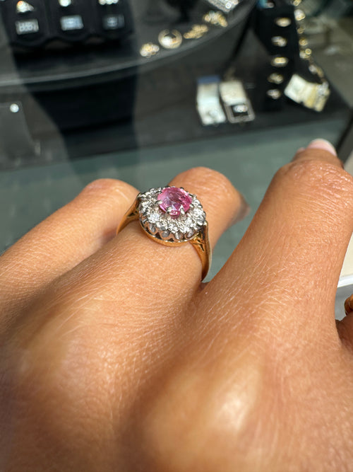 Ring with a pink gemstone on a finger, with blurred jewelry store background