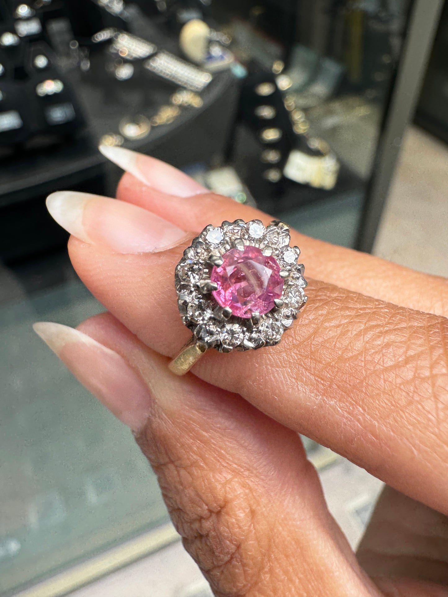 Pink sapphire ring with gold setting on a hand, blurred jewelry store background