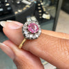Ring with a pink sapphire held on a hand against a blurred jewelry store background