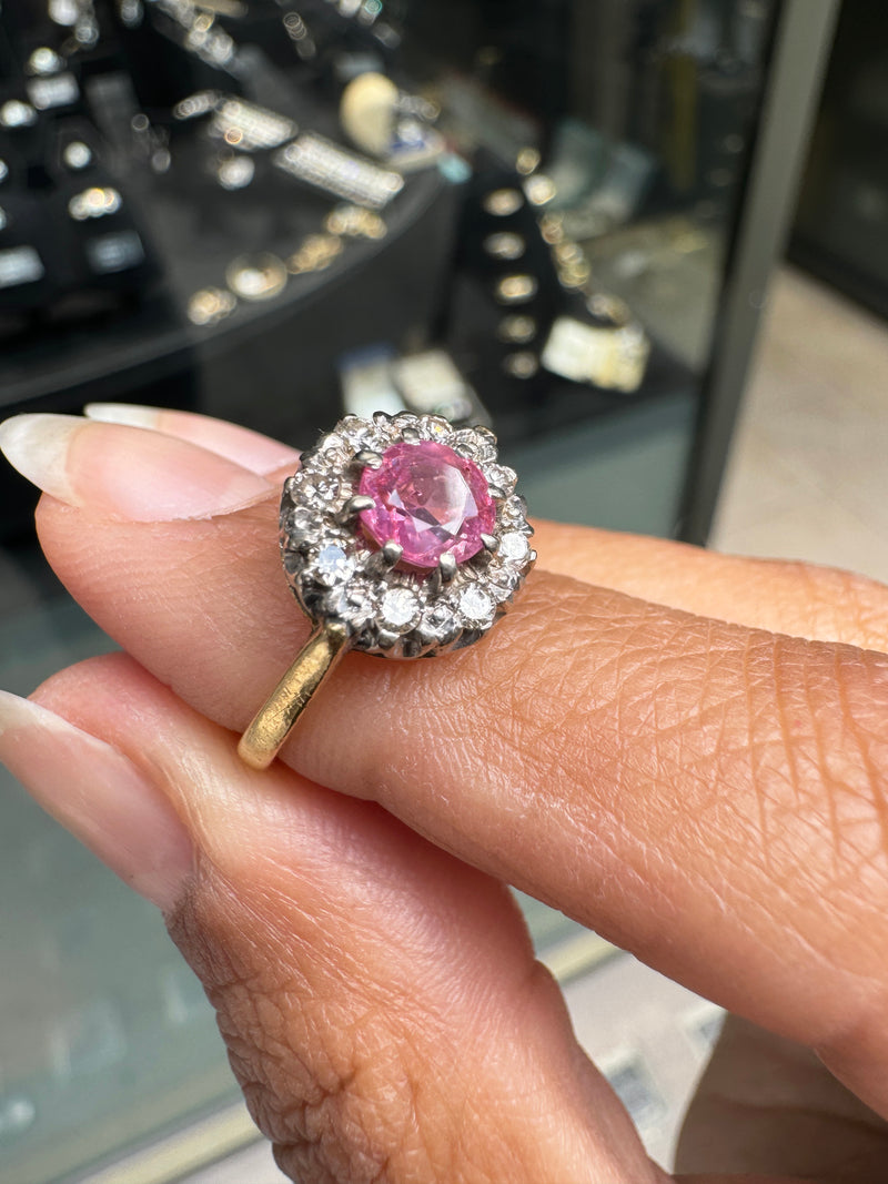Ring with a pink sapphire held on a hand against a blurred jewelry store background