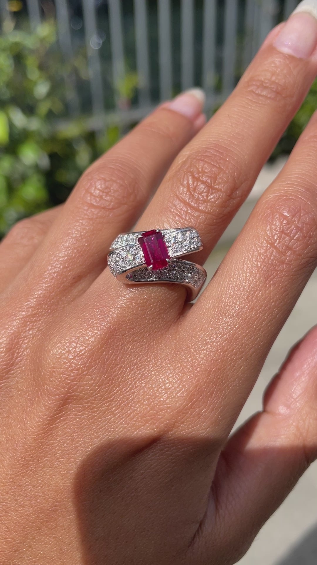 18ct white gold twisted ribbon dress ring with 1.04ct emerald cut ruby centre and 1.30ct round brilliant cut diamonds inlaid in two rows on hand