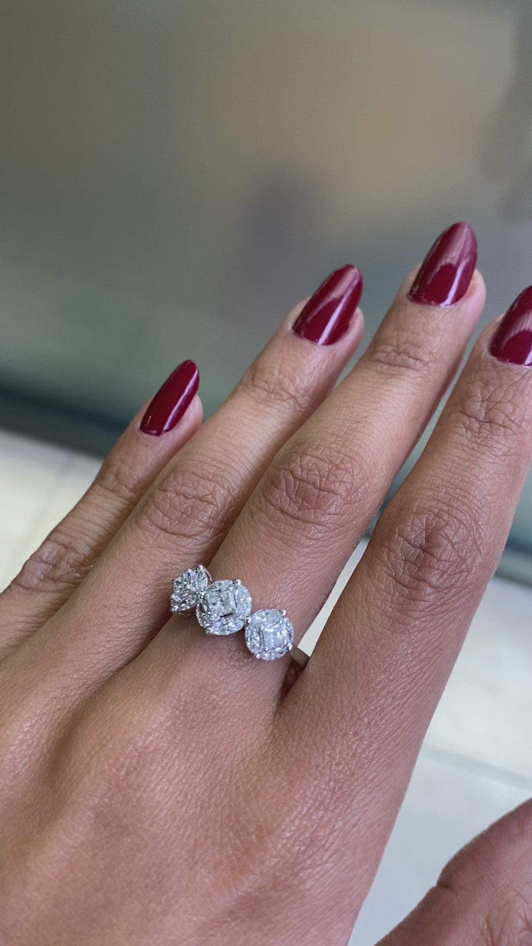 An 18 carat white gold trilogy diamond cluster engagement ring with three circular diamond clusters and a princess cut diamond in the center, set in a white gold band on hand 
