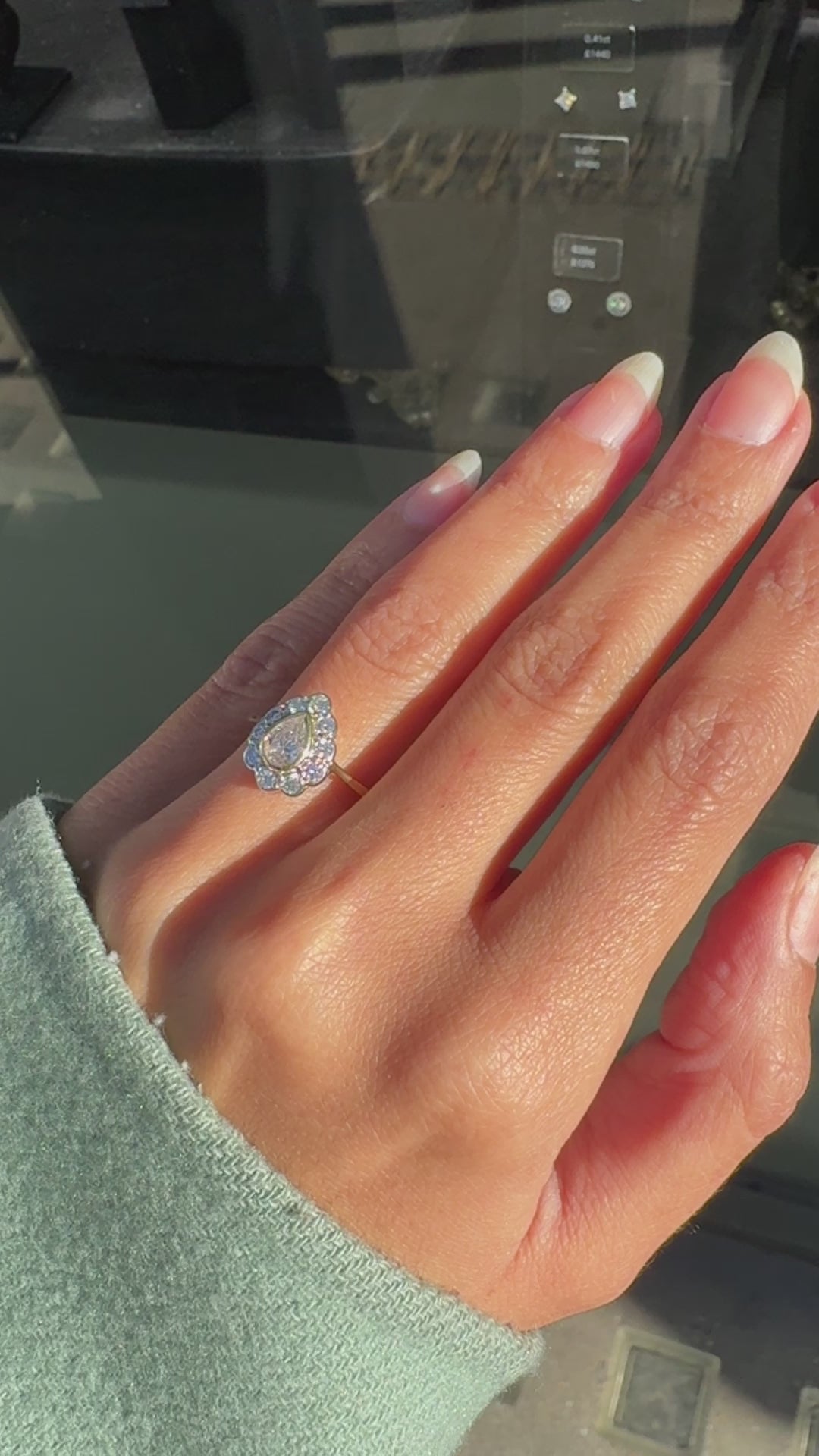 An 18 carat white and yellow gold pear shape diamond coronet cluster engagement ring with a central diamond surrounded by a halo of round brilliant cut diamonds on hand