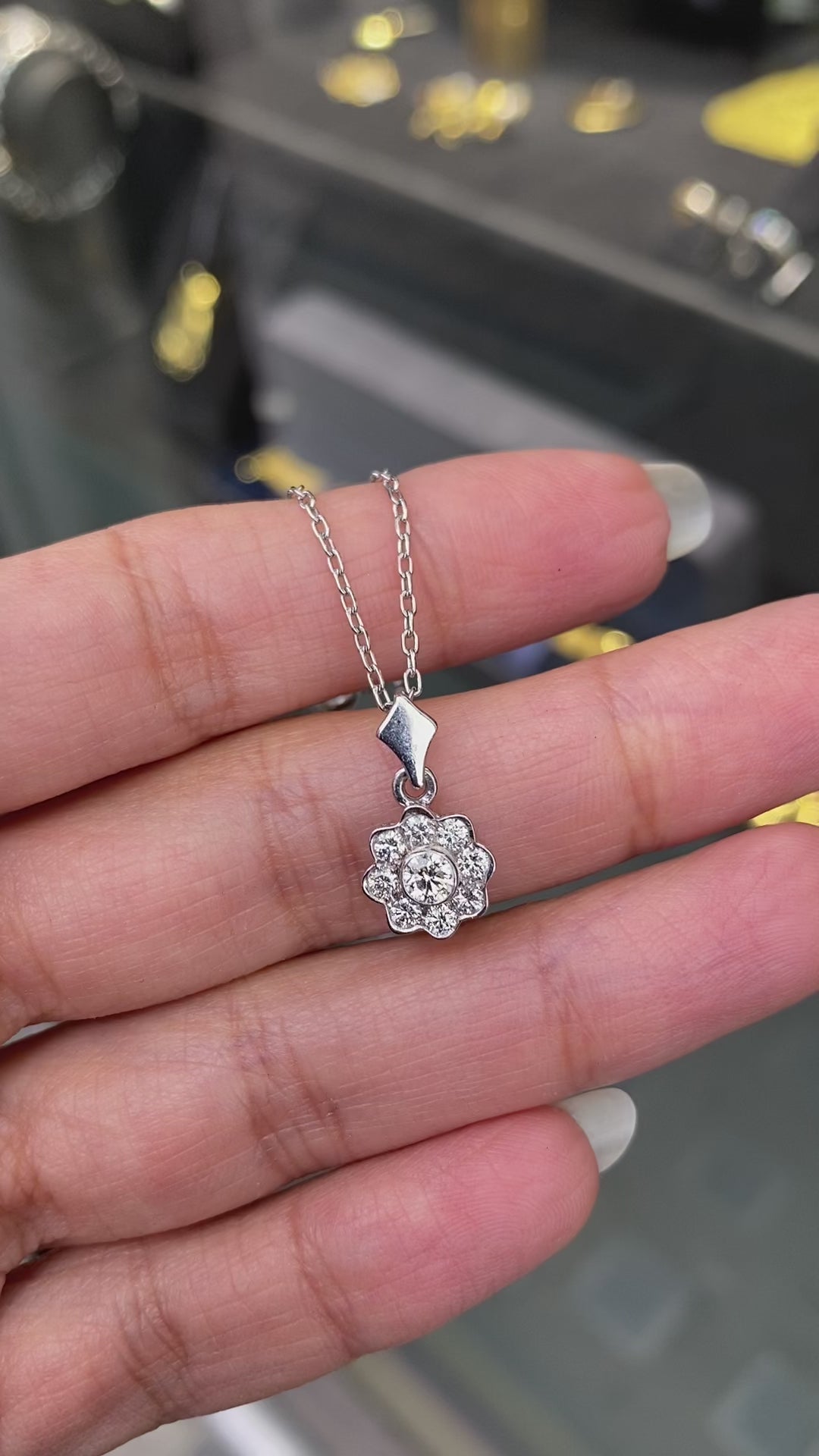 Video of a 0.45 carat diamond flower cluster pendant crafted in 18 carat white gold, round brilliant cut diamonds arranged in a floral design, suspended from a delicate white gold chain. on hand