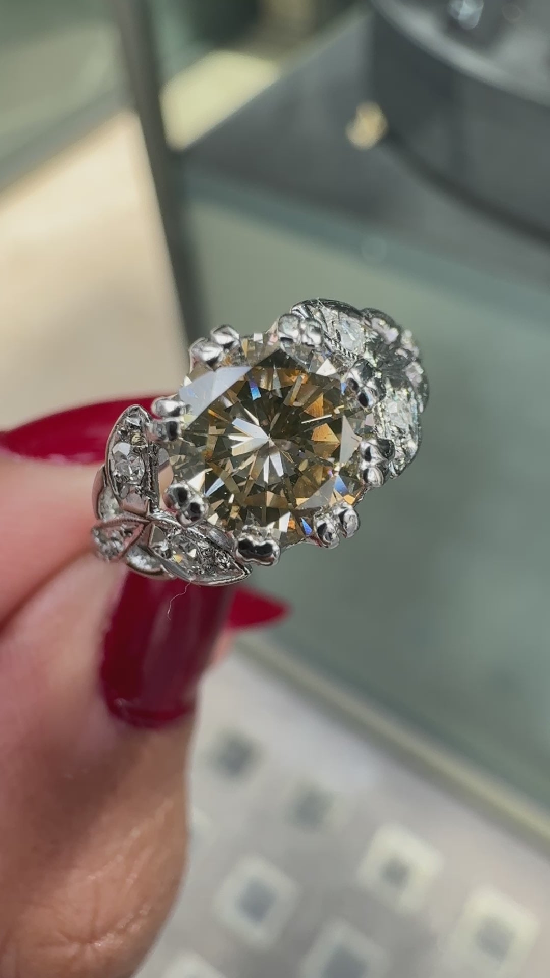 A vintage platinum engagement ring with a central 1.18ct fancy brown round brilliant cut diamond and three rose cut diamonds on either side, set in leaf designed pierced shoulders on hand