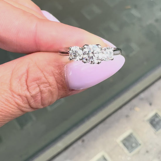 A platinum engagement ring with a central round brilliant cut diamond and two smaller round cut diamonds on the sides, set in an open-work gallery on hand.