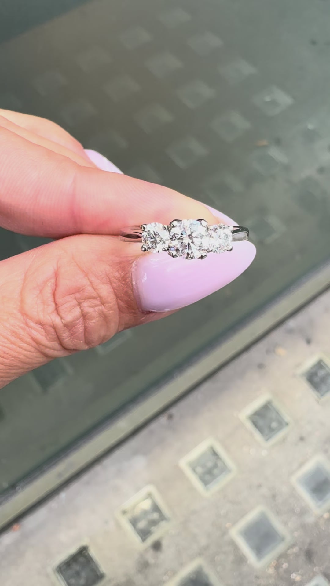  A platinum engagement ring with a central round brilliant cut diamond and two smaller round cut diamonds on the sides, set in an open-work gallery on hand.