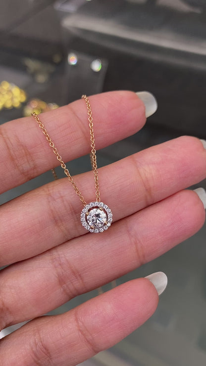 Video of a 18 carat rose gold halo cluster pendant featuring a round brilliant cut diamond center stone with a halo of smaller round diamonds, suspended on a slender gold chain. on hand
