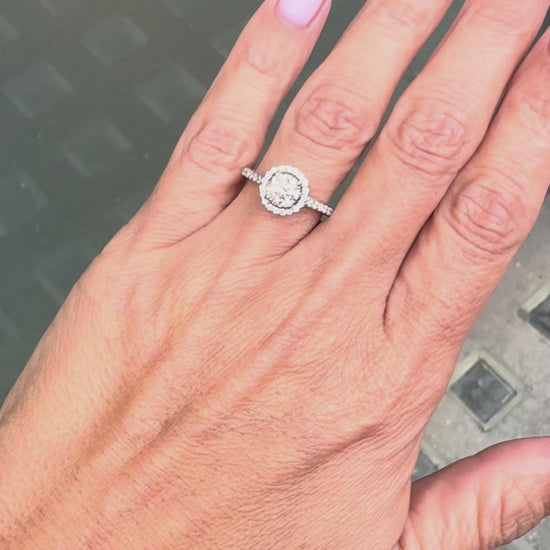 0.70ct E VS1 diamond halo cluster engagement ring in platinum with round brilliant cut centre stone, halo and diamond shoulders on hand