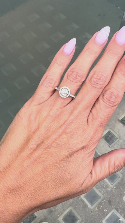 video of a 0.70ct E VS1 diamond halo cluster engagement ring in platinum with round brilliant cut centre stone, halo and diamond shoulders on hand