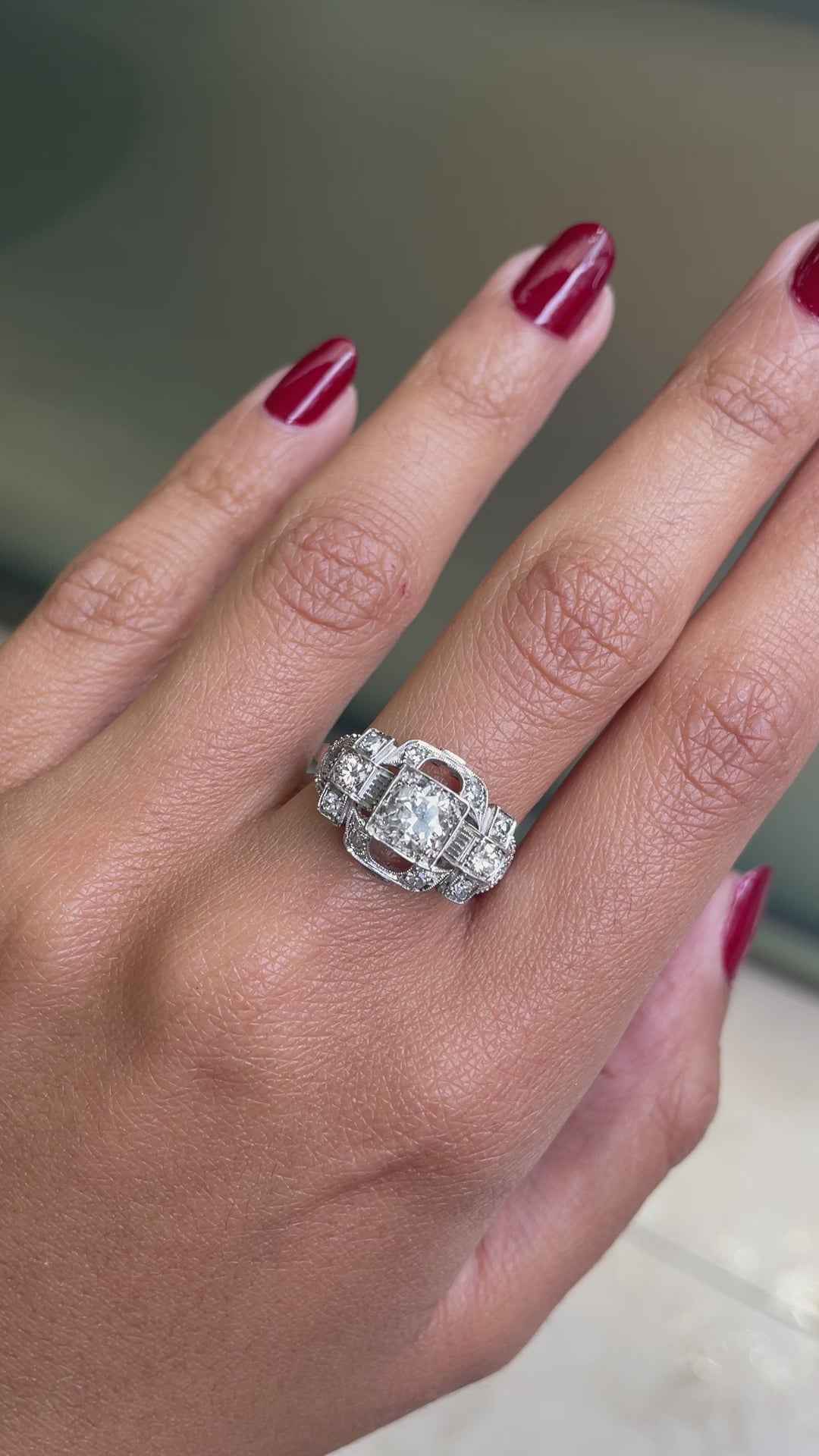An Art Deco style engagement ring with a central old cut diamond and additional diamonds set in a platinum mount with open work detailing on hand