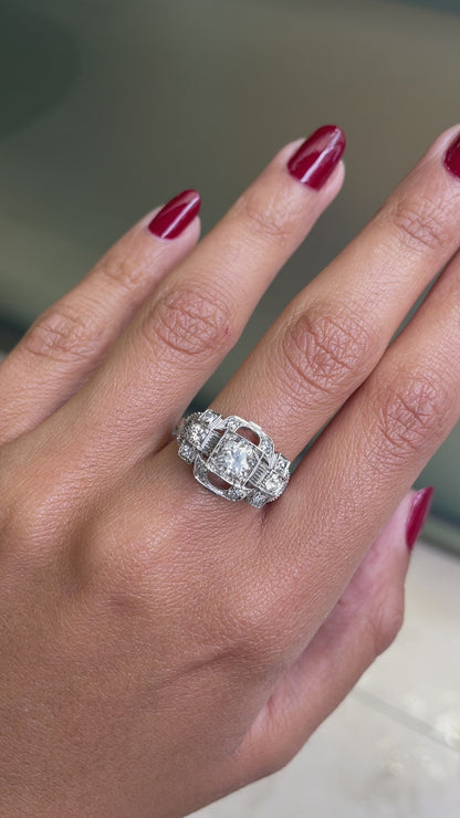 An Art Deco style engagement ring with a central old cut diamond and additional diamonds set in a platinum mount with open work detailing on hand