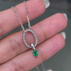 An 18 carat white gold oval pendant featuring a central emerald, surrounded by round brilliant cut diamonds set in a claw-like design.